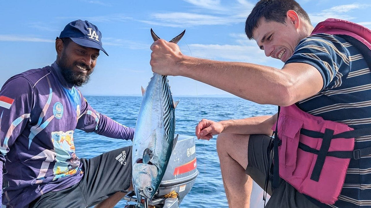Two men on a boat holding a large fish, with the ocean and sky in the background.