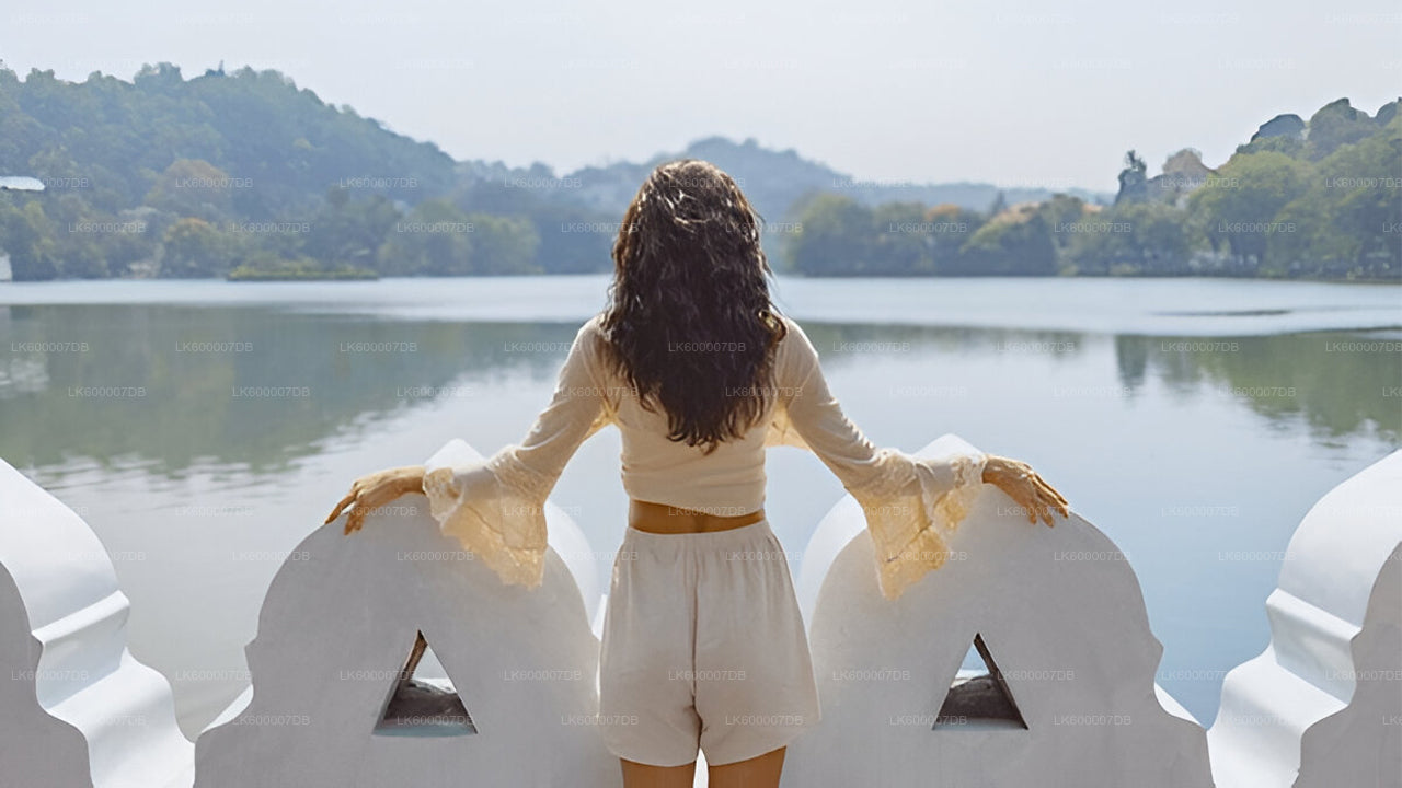 Woman in a white outfit standing on a decorative stone bench by a lake with trees in the background