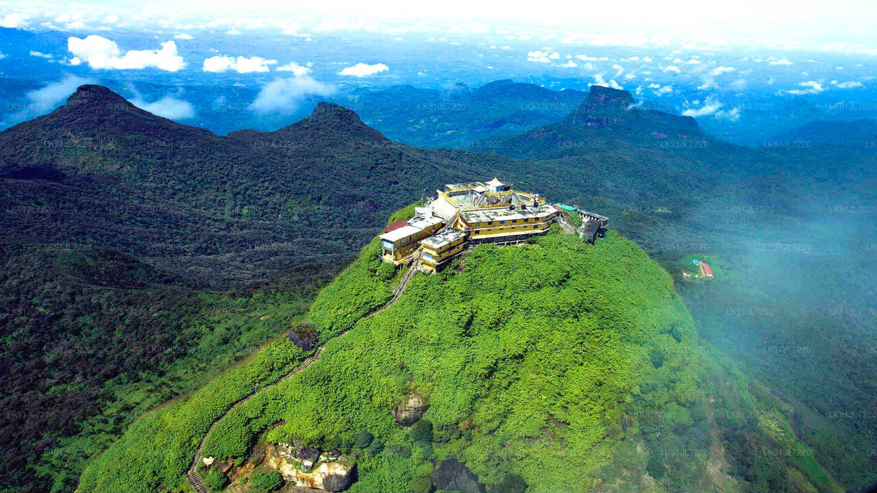 A scenic view of Adam's Peak, a prominent mountain in Sri Lanka, with a structure on top and surrounded by misty mountains in the background.